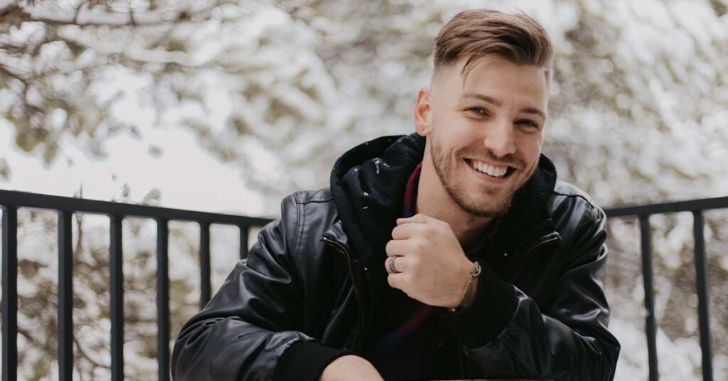 Smiling young man in black jacket out in the snow.