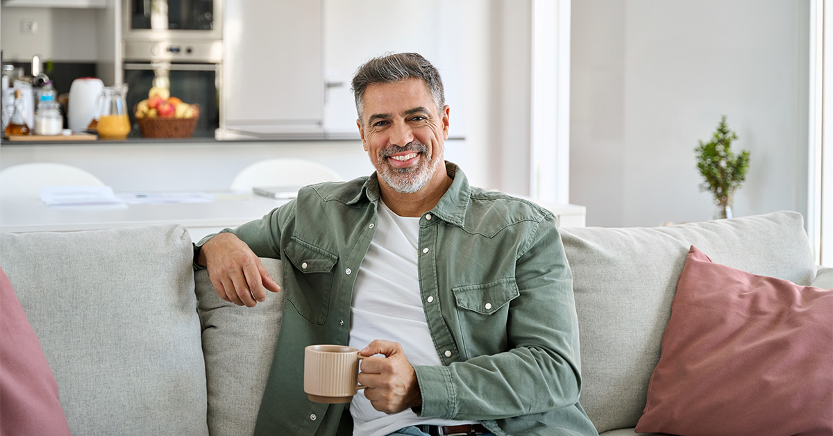 Smiling man on couch drinking from a mug.