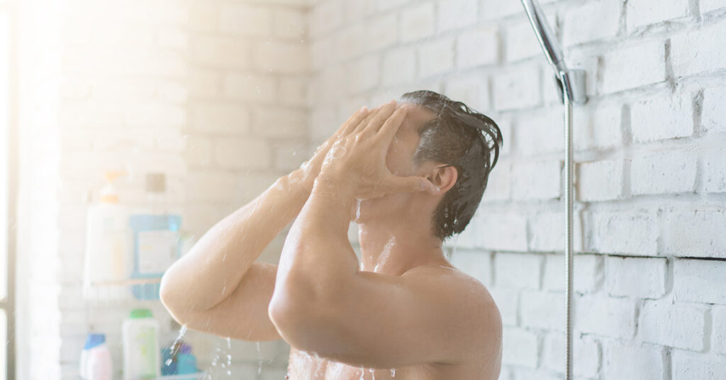 Man taking a hot shower and covering is face with his hands.