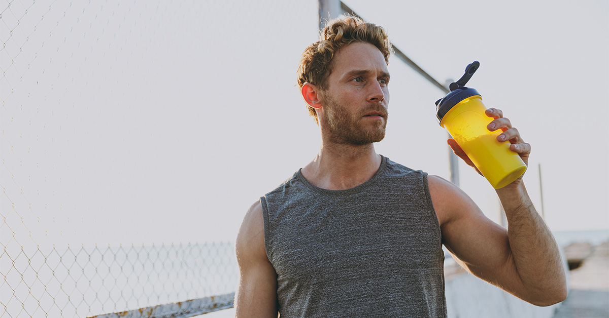 Man in a dark gray tank top drinking from a translucent yellow bottle,